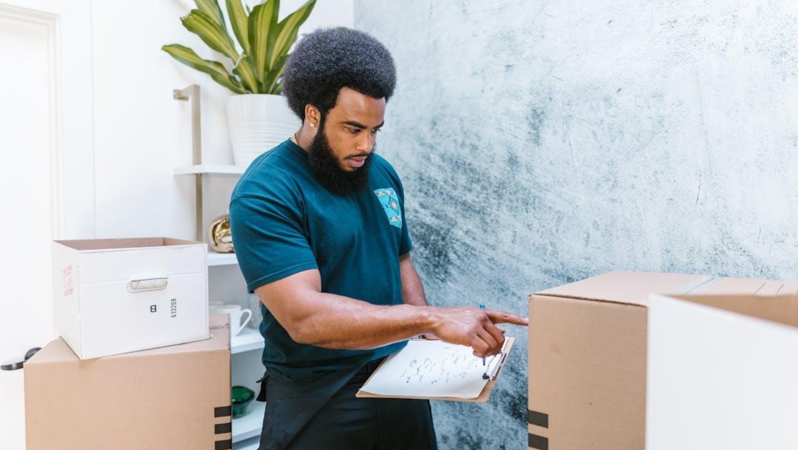 A moving company employee checking cardboard box while holding notes